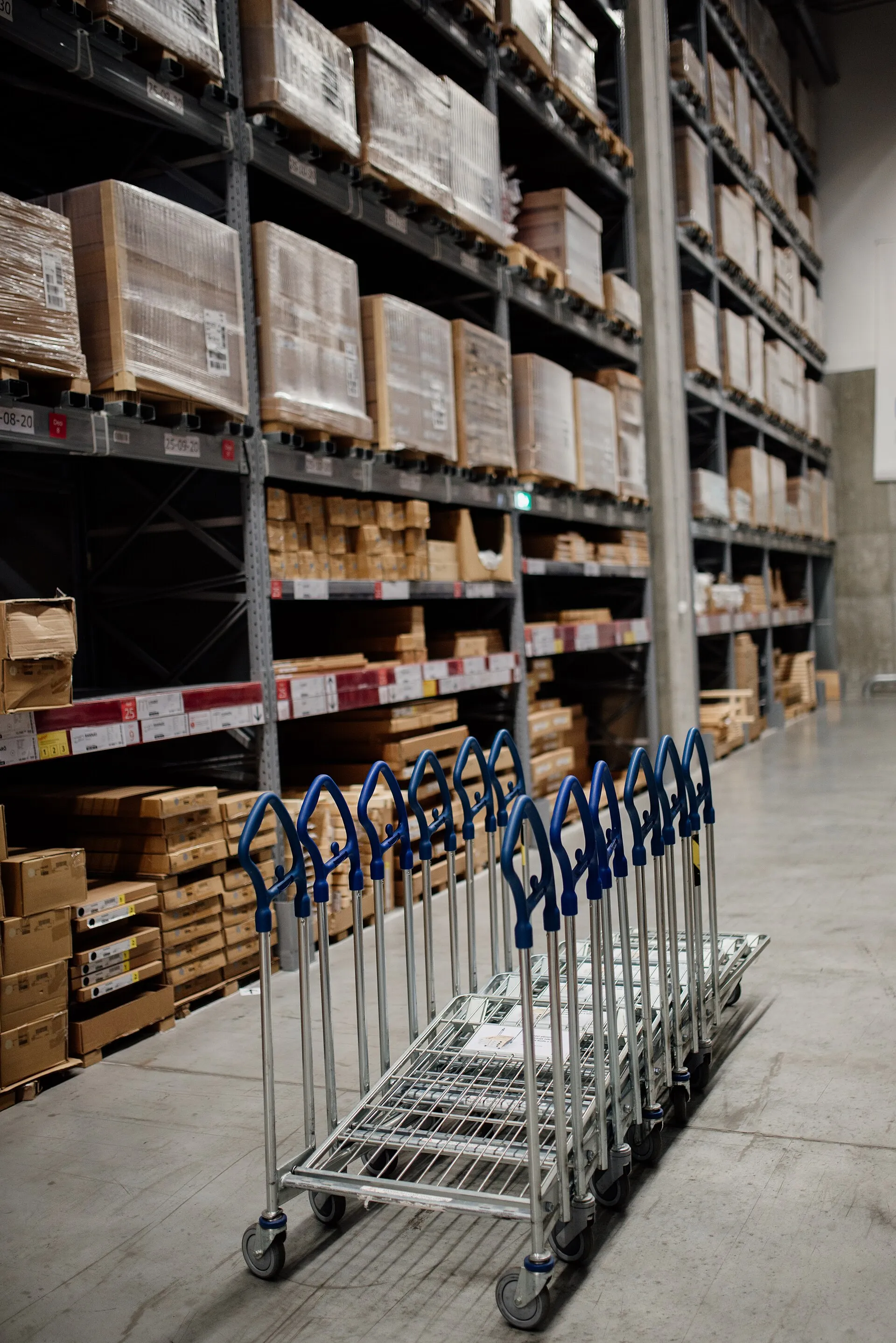 A warehouse aisle of boxed stock on high shelves, with a row of picking carts